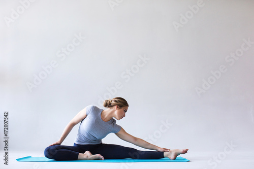 Fotomural Young beautiful woman in sportswear doing stretching while sitting on the floor on yoga mat
