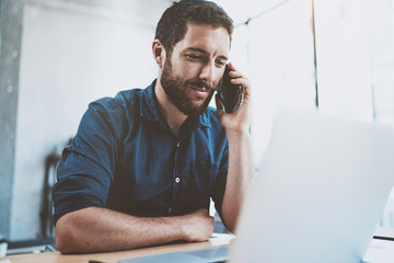 Smiling businessman using smartphone at office and making notes.Blurred background.Horizontal.