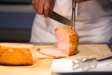 Chef using folk picking and cutting or slicing piece of pork on wooden board in hotel food restuarant,Professional cuisine concept