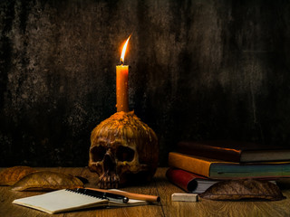 A wizard working desk with candle on the human skull, books of magic, note book and stationary.