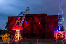 Two Illuminated Cranes In Front Of Old Warehouse