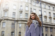 © shurkin_son - Picture of fashionable elegant young female wearing trendy striped coat and grey scarf standing in urban setting with apartment building in background. People, modern lifestyle and fashion concept