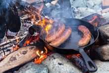 Cooking Sausages In Cast Iron Skillet On Campfire While Camping. Good And Positive Campfire Food.