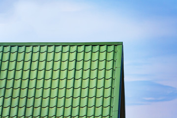 Fragment of a green metal tile roof a background of cloudy sky