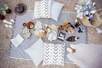 Top view on picnic blanket layout with fresh artisan bread, wine, cheese, fruits and oysters, with wooden tray and pillows with candles around for romantic amorous style