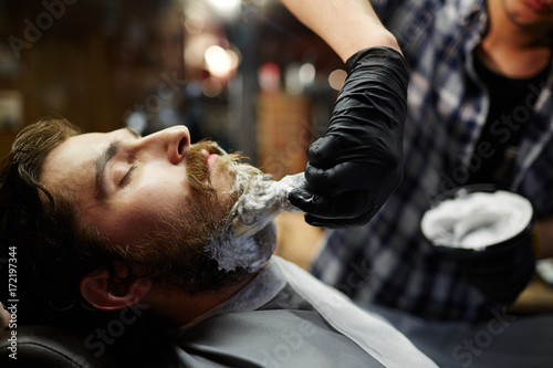 Fotografie, Obraz Shaving ritual in barbershop - barber applying foam before procedure