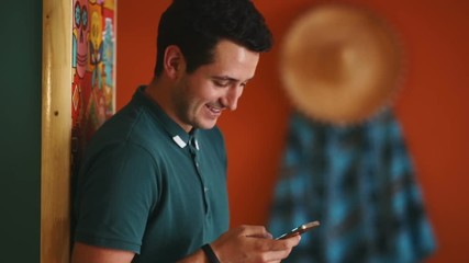 Young cheerful attractive man laughing smiling leaning colorful wall picture mask using smartphone happy guy searching internet looking screen sombrero mexico mexican restaurant red warm ethnic online