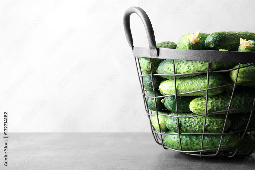 Many green fresh cucumbers in metal basket on gray table