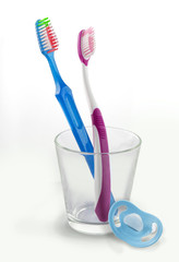 Two toothbrushes in a glass with pacifier