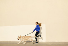 Side View Of A Woman Running With Her Dog On The Street.