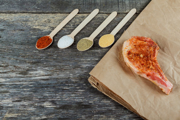 Raw pork steaks on wooden board with herbs, garlic, spices and tomatoes ready for cooking.