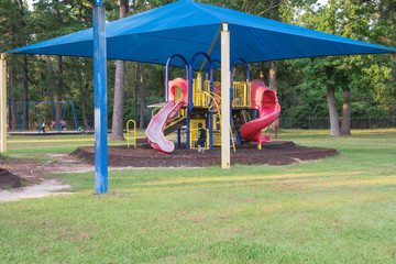 Sun shade playground at grassy public park in Houston, Texas, US. Safe, comfort covered playground for kids play all day. Sail fabric canopy blocks up to 90% harmful UV rays. Unidentified kids playing