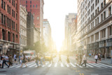Fototapeta Miasto - Groups of people walking across a busy crosswalk intersection in New York City with the glow of the sun in the background