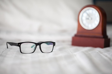 Glasses and alarm clock on the white bed