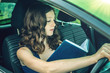 © Artem - Woman driver reading a book in the car. Distracted and dangerous driving. The traffic violation.