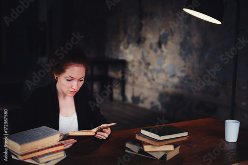 indoor portrait of beautiful redhead woman learning or reading books in university or library