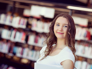 Wall Mural - Happy female student holding books at the library