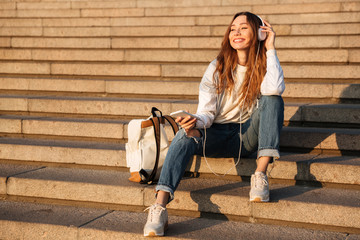 Poster - Smiling brunette woman in autumn clothes sitting on stairs