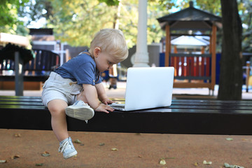 Wall Mural - Little boy is sitting on the bench with laptop