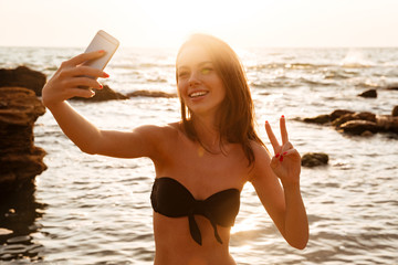 Wall Mural - Joyful brunette woman in bikini making selfie on her smartphone