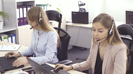 The operator of the hotline with headsets, sit at the computer in the office and advise clients. Workers call-center, a woman talking to customers. She prints on the computer and answers questions.