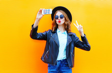 Fashion Woman Is Taking A Picture On A Smartphone In Black Rock Jacket On Colorful Orange Background