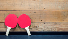 2 Red Ping Pong Paddles Leaning Against A Wooden Wall With Copy Space