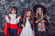 © kanashkin - Children in scary Halloween costumes stand against a wall with drawings.