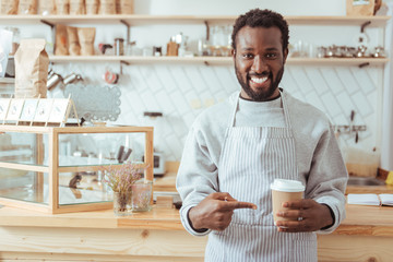 Wall Mural - Charming barista pointing at cup of coffee