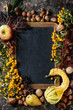 Frame from autumn berries, pumpkin, leaves and nuts with empty vintage chalkboard over brown concrete background. Top view with space for text. Fall harvest concept.