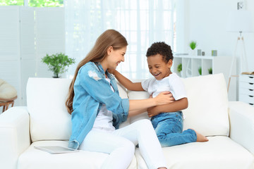 Wall Mural - Happy mother with adopted African-American boy sitting on couch at home