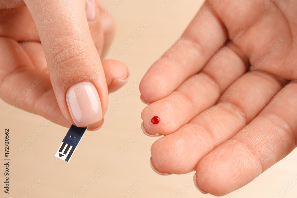 Woman's hands using glucose test strip on light background. Diabetes concept