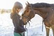 Frau Reiterin streichelt Hannoveraner Pferd vor Schneelandschaft