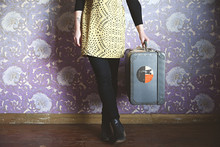 Anonymous Female Holding A Vintage Suitcase In Front Of Retro Wallpaper