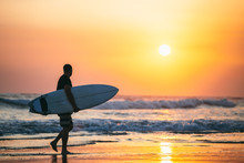 Man Carrying Surfboard Along Beach At Sunset