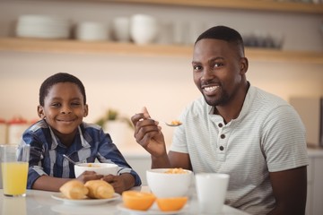 Smiling father and son having breakfast in kitchen