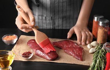 Canvas Print - Woman applying oil on raw steak with silicone brush in kitchen