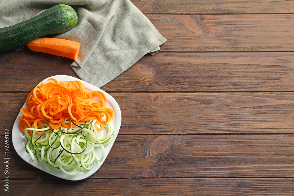 Plate with zucchini and carrot spaghetti on wooden background