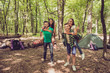 © deagreez - Camp in the sunny wood, tent and backpacks. Two lovely couples, guys are piggybacking their girlfriends, happy, smiling