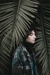 © Nicole Mason/Stocksy - Young woman standing in palm tree leaves at sunset