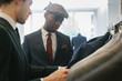 © Julien L. Balmer/Stocksy - Men's Fashion Shopping - Caucasian Shop Assistant Showing Suits to Young Black Customer