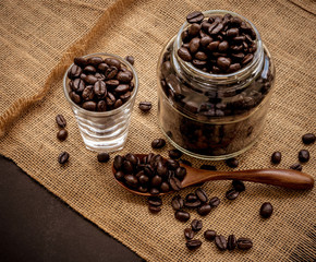 Wall Mural - Coffee bean grain in a glass bottle on black table with sack fabric