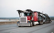 © vit - Red classic big rig semi truck with car hauler trailer running by highway to point of loading cars for delivery