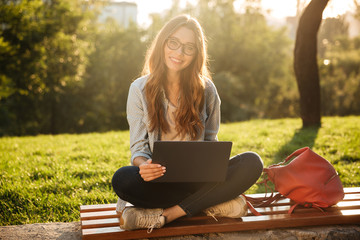 Canvas Print - Smiling brunette woman in eyeglasses sitting on bench