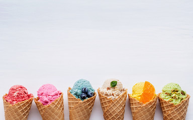 Fototapete - Various of ice cream flavor in cones blueberry ,strawberry ,pistachio ,almond ,orange and cherry setup on white wooden background . Summer and Sweet menu concept.