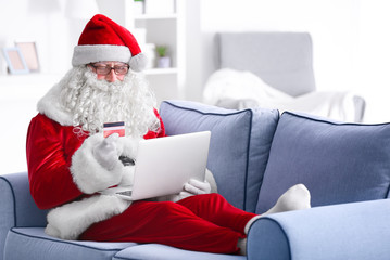 Wall Mural - Santa Claus with laptop and credit card on sofa at home