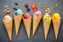 Various Of Ice Cream Flavor In Cones Blueberry ,strawberry ,pistachio ,almond ,orange And Cherry Setup On Dark Stone Background . Summer And Sweet Menu Concept.