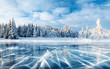 canvas print picture - Blue ice and cracks on the surface of the ice. Frozen lake under a blue sky in the winter. The hills of pines. Winter. Carpathian, Ukraine, Europe.