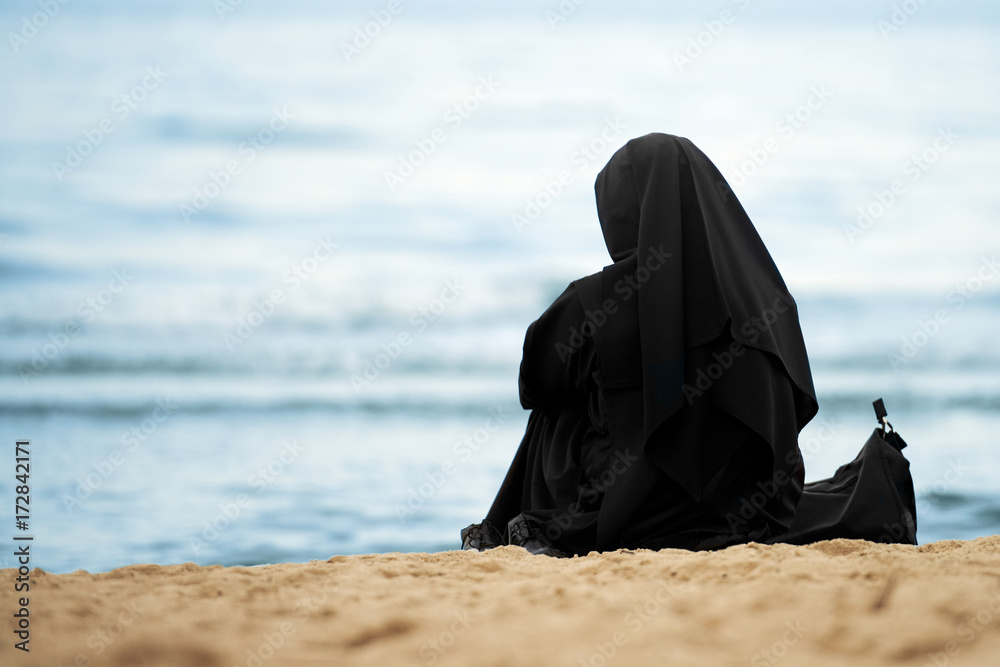Muslim woman with black clothes sitting on the beach Stock Photo | Adobe  Stock