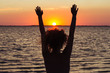 The girl raising her hands to the red sunset at sea, enjoying nature and freedom